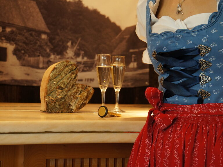 Eine weibliche Bedienung in Tracht posiert vor einem Tisch mit zwei Sektgläsern