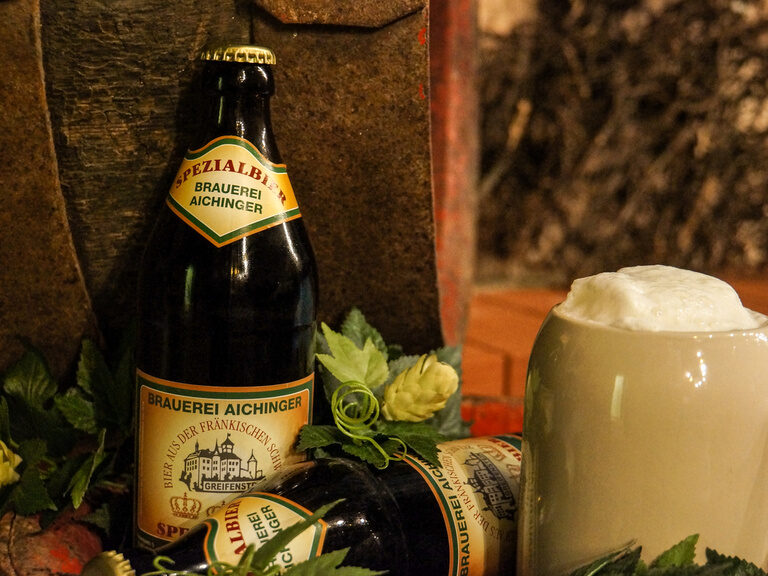 Ein Bierkrug und eine Flasche Bier der Brauerei Aichinger in Bamberg stehen auf einem Tisch