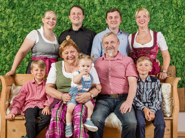 Die Gastgeberfamilie Regus sitzt lächelnd auf einer Bank vor einer grünen Wand.