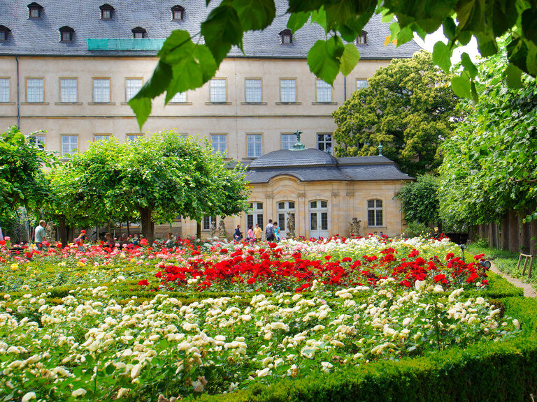 Ein blühender Garten mit Bäumen und Blumen vor einem historischen Gebäude in Bamberg