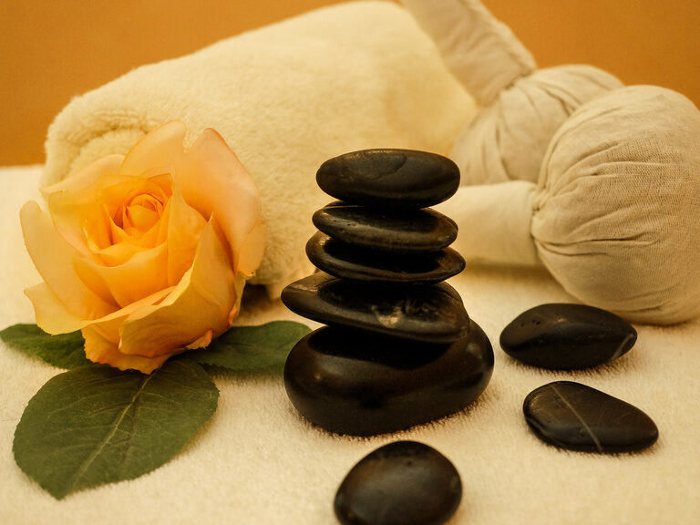 Verschiedene Massage-Utensilien, wie Hot-Stone-Massagesteine liegen auf einem Handtuch