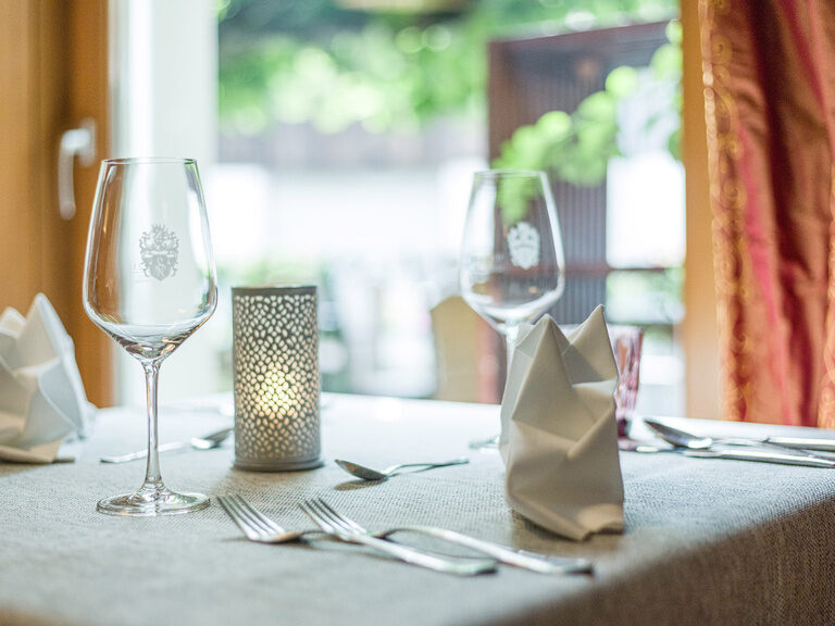 Ein Restaurant-Tisch im Landhaus Sponsel-Regus in Franken ist mit stilvollem Geschirr und Weingläsern eingedeckt.